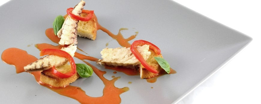 Antipasto di sgombro marinato con peperoni, ginepro, timo e pomodorini su crostini di pane.